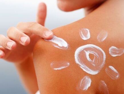 Close-up of a person applying suncream on their shoulder with a sun design drawn with the cream.