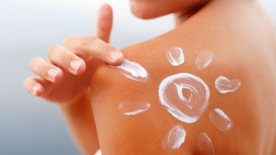 Close-up of a person applying suncream on their shoulder with a sun design drawn with the cream.